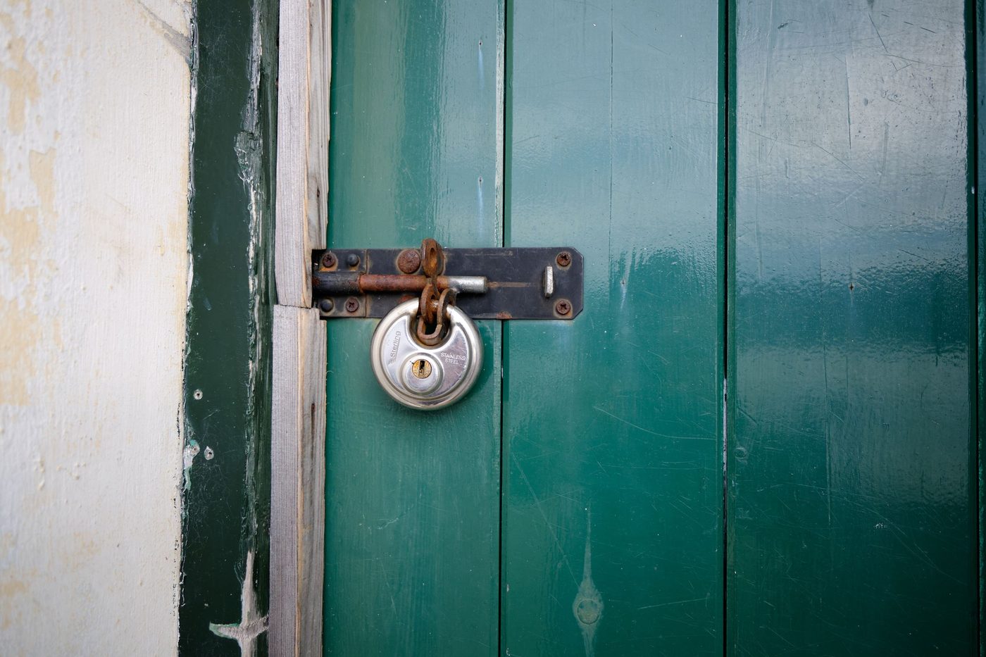 A round silver padlock closes a bolt on a green painted wooden door