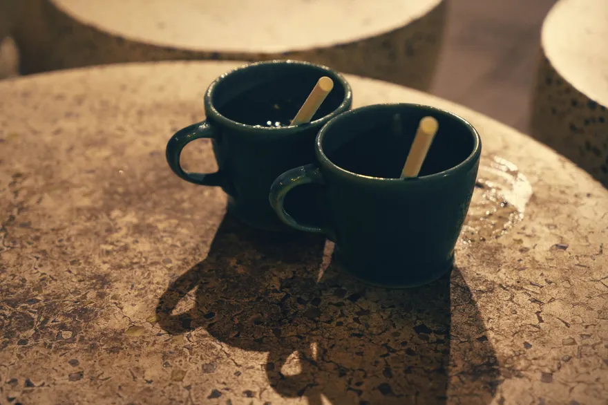 Two dark coffee cups side by side on a stone cafe table in warm light