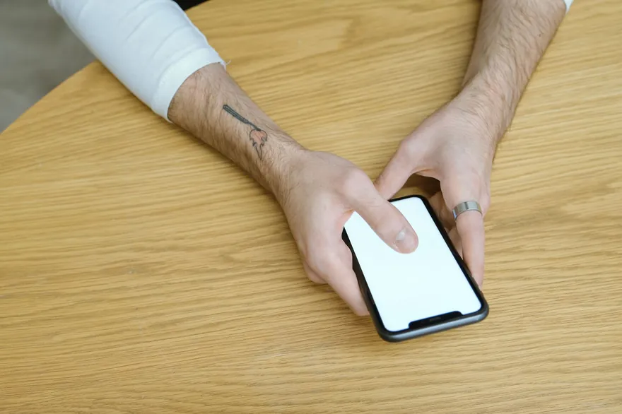 Two hands hold a phone with a blank screen above a wooden table