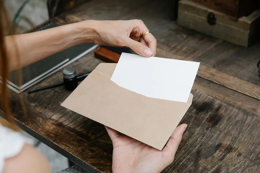 Hands taking a blank card out of a brown paper envelope over a worn wooden desk
