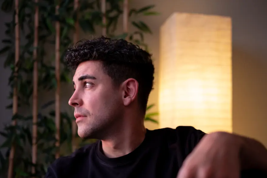 A man in a dark T-shirt looking away from the camera, lit by a warm paper floor lamp