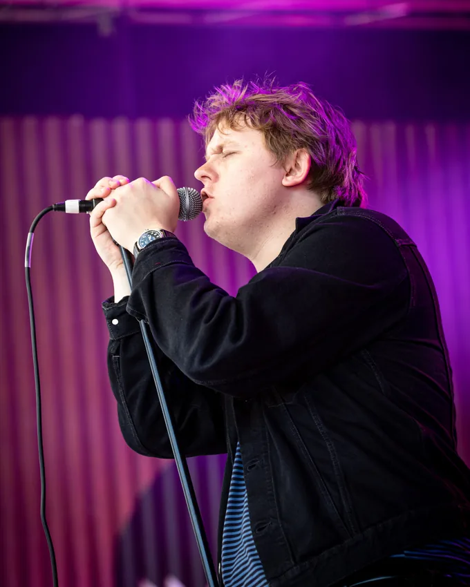 Lewis Capaldi singing under purple stage lights in 2019