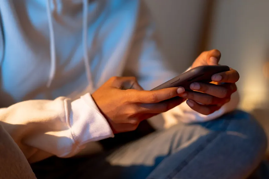 Hands holding a phone low over the lap of a person sitting on a sofa